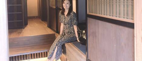 A traditional Japanese interior with sliding doors, a wooden floor, and a person sitting on a bench.