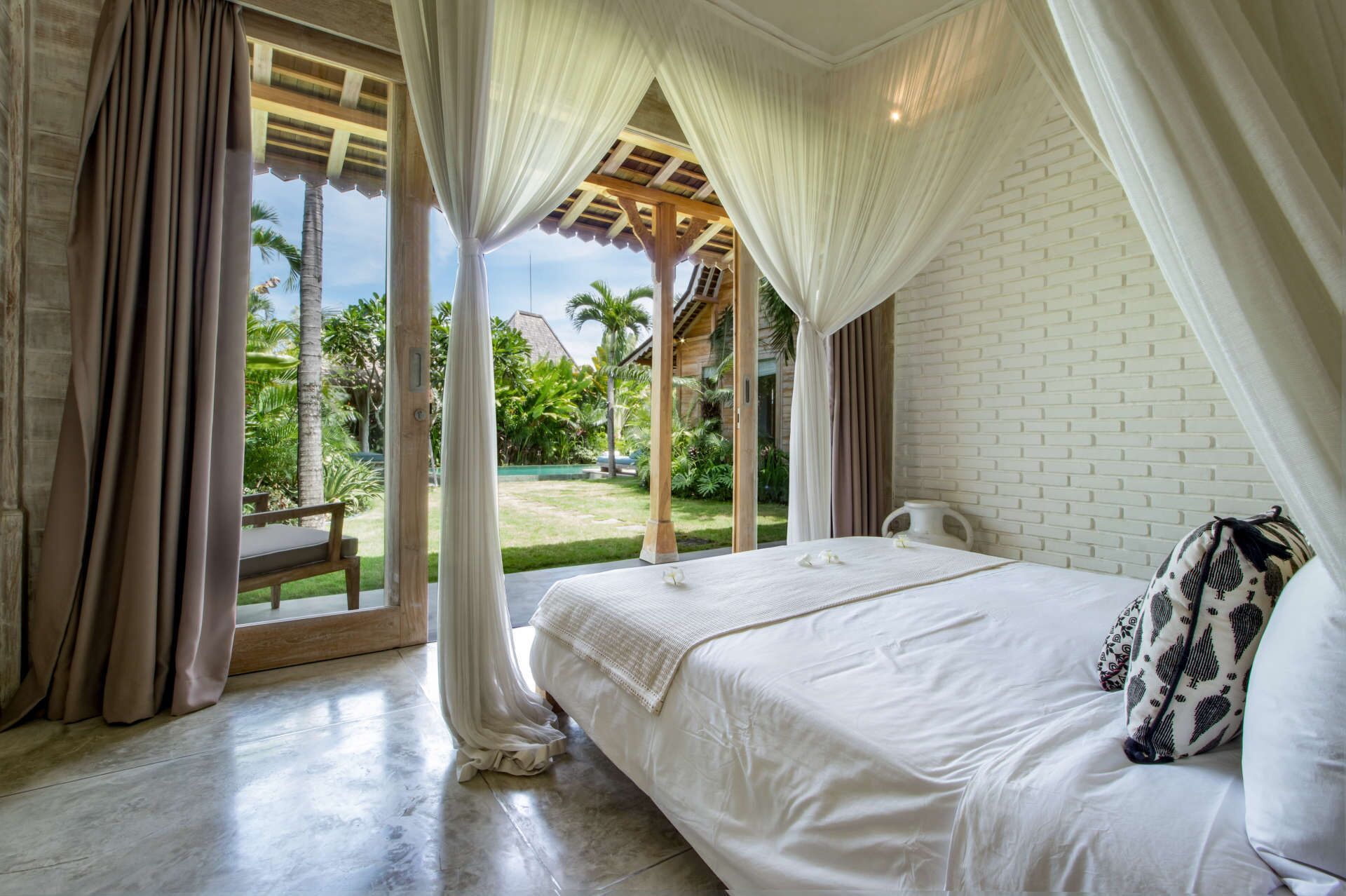 Un dormitorio con una cama grande, cortinas blancas y vista a un jardín.