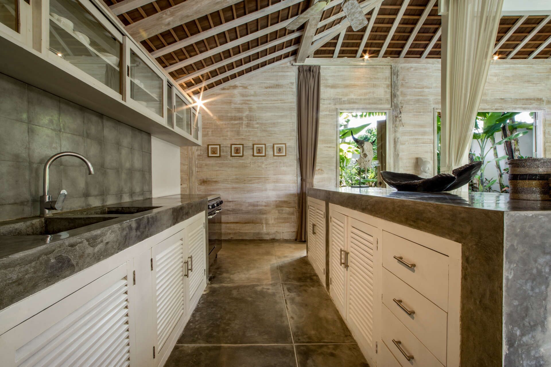 A kitchen with a large island, a built-in stove, and a window with a view of greenery.