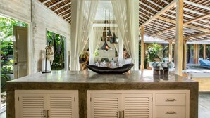 Un espacio interior amplio con techos altos, una isla central con una mesa y sillas, y vistas al exterior a través de grandes ventanales.