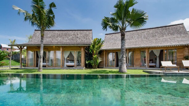 A resort with two wooden buildings, a clear pool, and palm trees.