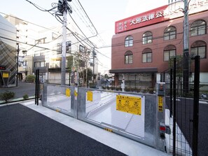 Een poort met een metalen hek en waarschuwingsborden, een rood gebouw met een bord in het Japans, en een heldere lucht.