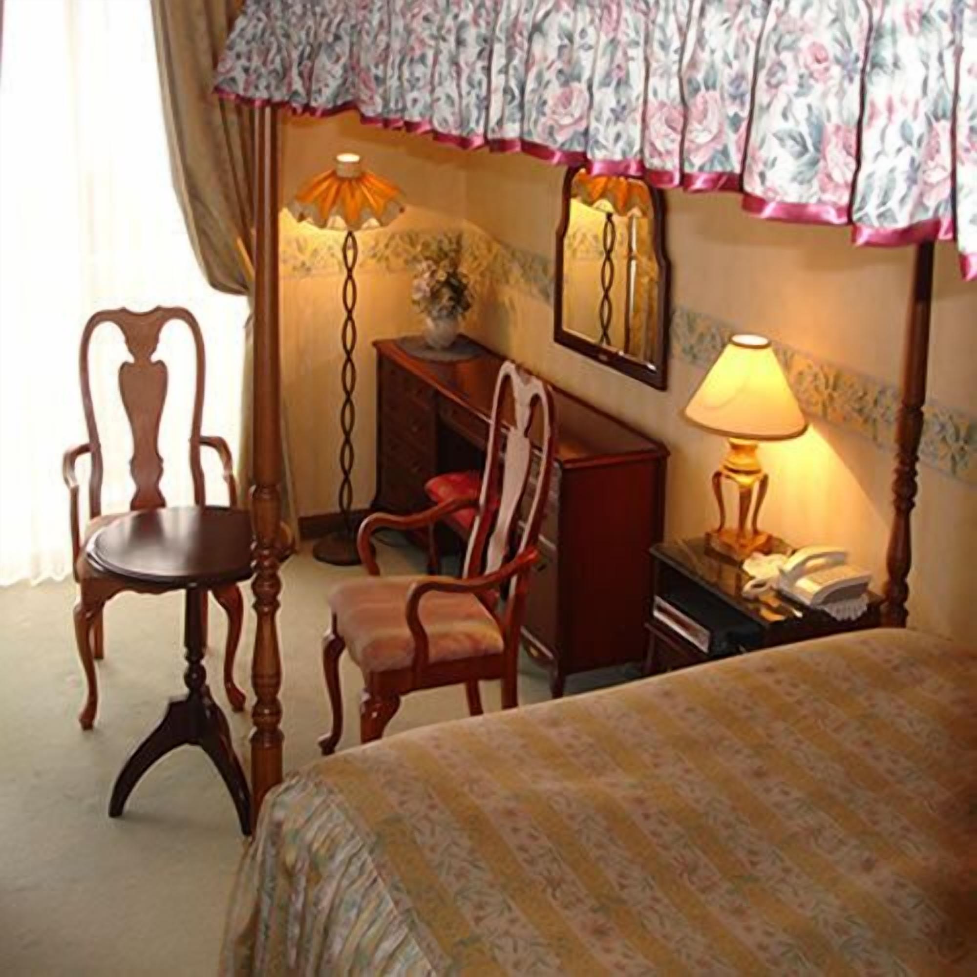 A hotel room with a bed, two chairs, a desk, a lamp, and a mirror.