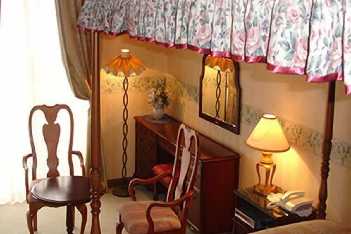 A hotel room with a bed, two chairs, a desk, a lamp, and a mirror.
