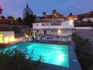 Una piscina con sillones de descanso y un patio cubierto.