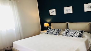 Habitación de hotel con una cama, dos almohadas, una mesita de noche, una lámpara y tres cuadros en la pared.