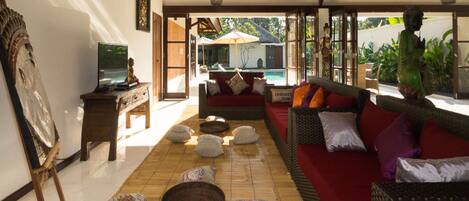 Amplia sala de estar con un sofá rojo, una mesa de centro de madera y un ventanal con vistas a una piscina.