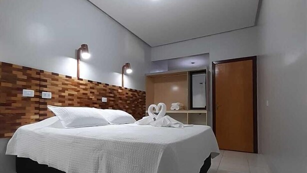 Une chambre d’hôtel moderne avec un lit, un mur décoratif en bois, un miroir et une porte.