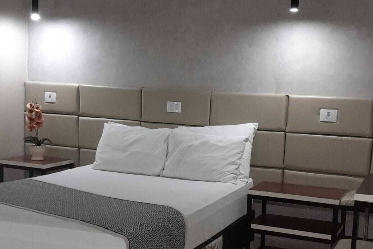 Una habitación de hotel moderna con una cama grande, una mesita de noche con un jarrón de flores y otra mesita con una lámpara.