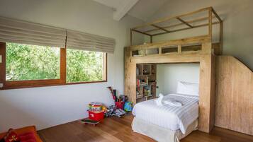 Una cama individual con estructura de madera, un escritorio pequeño y una ventana con vista a follaje.