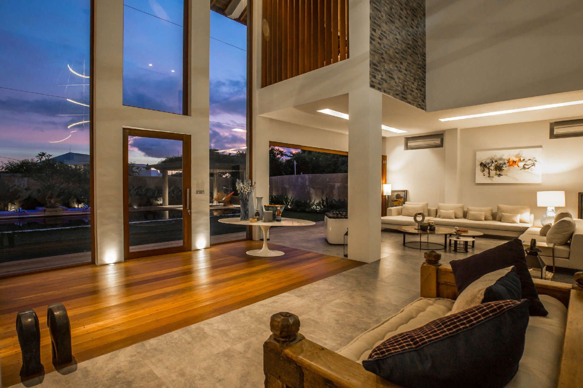 Un salón espacioso con un ventanal grande con vistas a un jardín, una zona de estar acogedora con sofá y sillones, y un diseño moderno de líneas depuradas.