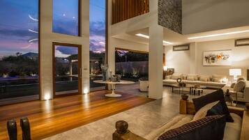 Un salón espacioso con un ventanal grande con vistas a un jardín, una zona de estar acogedora con sofá y sillones, y un diseño moderno de líneas depuradas.