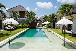 Une piscine entourée de palmiers et de bâtiments modernes, avec des chaises longues et des parasols.