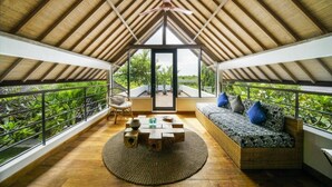 Una habitación en el ático con techo alto, vigas de madera, un ventanal grande, un sofá, una silla y una mesita con objetos decorativos.