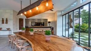 Una cocina moderna con una isla grande de madera, un comedor con sillas y vistas al exterior a través de amplios ventanales.