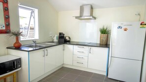 A compact kitchen with white cabinets, a black countertop, a stainless steel sink, a built-in oven, and a white refrigerator. - Beautiful & Bright Studio APT (Auckland)
