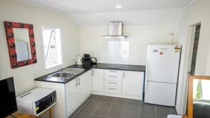 A compact kitchen with a sink, stove, and refrigerator, featuring a window and a decorative mirror. - Beautiful & Bright Studio APT (Auckland)