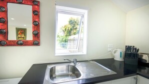 A kitchen with a black countertop, stainless steel sink, and a window with a view of greenery. - Beautiful & Bright Studio APT (Auckland)