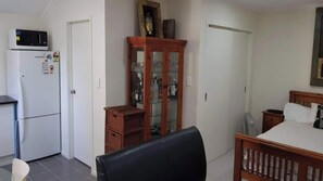 A compact room with a bed, a small desk, a refrigerator, and a cabinet with glass doors. - Beautiful & Bright Studio APT (Auckland)
