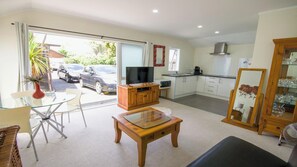 A living room with a TV, wooden furniture, a glass table, a dining area with chairs, and a kitchen with cabinets and a microwave. - Beautiful & Bright Studio APT (Auckland)