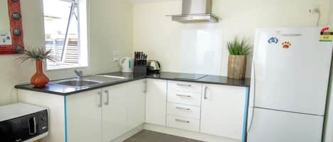 A compact kitchen with white cabinets, a black countertop, a stainless steel sink, a built-in oven, and a white refrigerator.