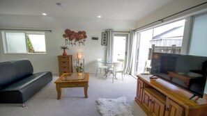 A living room with a black sofa, a wooden coffee table, a glass dining table with chairs, a TV on a wooden cabinet, and a decorative wall hanging. - Beautiful & Bright Studio APT (Auckland)