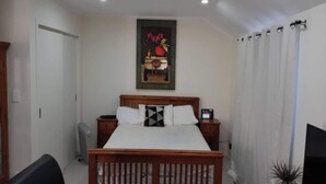 A bedroom with a wooden bed, two bedside tables, a wall-mounted TV, and a painting above the bed. - Beautiful & Bright Studio APT (Auckland)