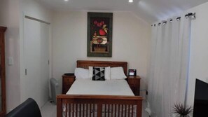 A bedroom with a wooden bed, two bedside tables, a wall-mounted TV, and a painting above the bed. - Beautiful & Bright Studio APT (Auckland)