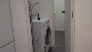 A small laundry room with a washing machine and a dryer, a door, and tiled flooring. - Beautiful & Bright Studio APT (Auckland)