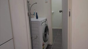 A small laundry room with a washing machine and a dryer, a door, and tiled flooring. - Beautiful & Bright Studio APT (Auckland)
