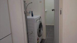 A small laundry room with a washing machine and a dryer, a door, and tiled flooring. - Beautiful & Bright Studio APT (Auckland)