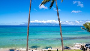 A beach view with palm trees, clear blue water, and a distant mountain. - Newly upgraded kitchen with oceanfront views (Lahaina)