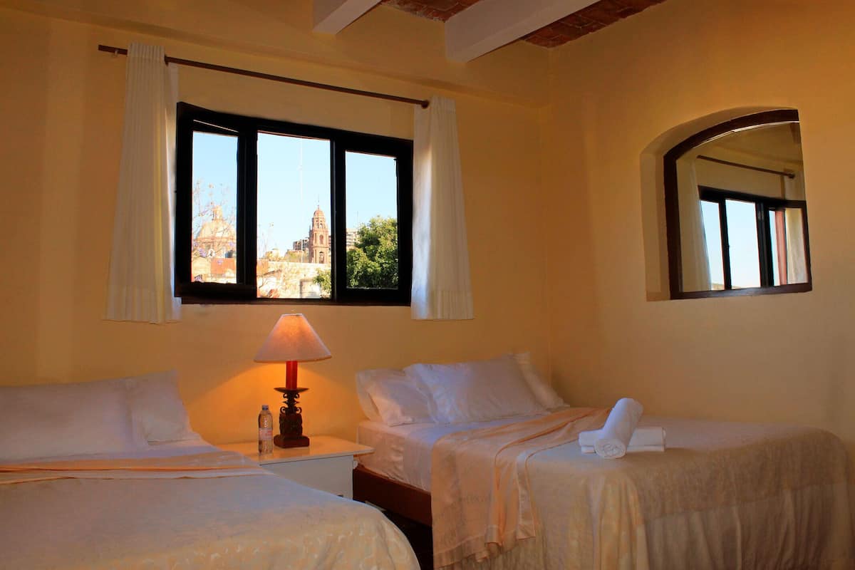 Une chambre d’hôtel avec deux lits, une table de chevet avec une lampe et une fenêtre donnant sur un immeuble.