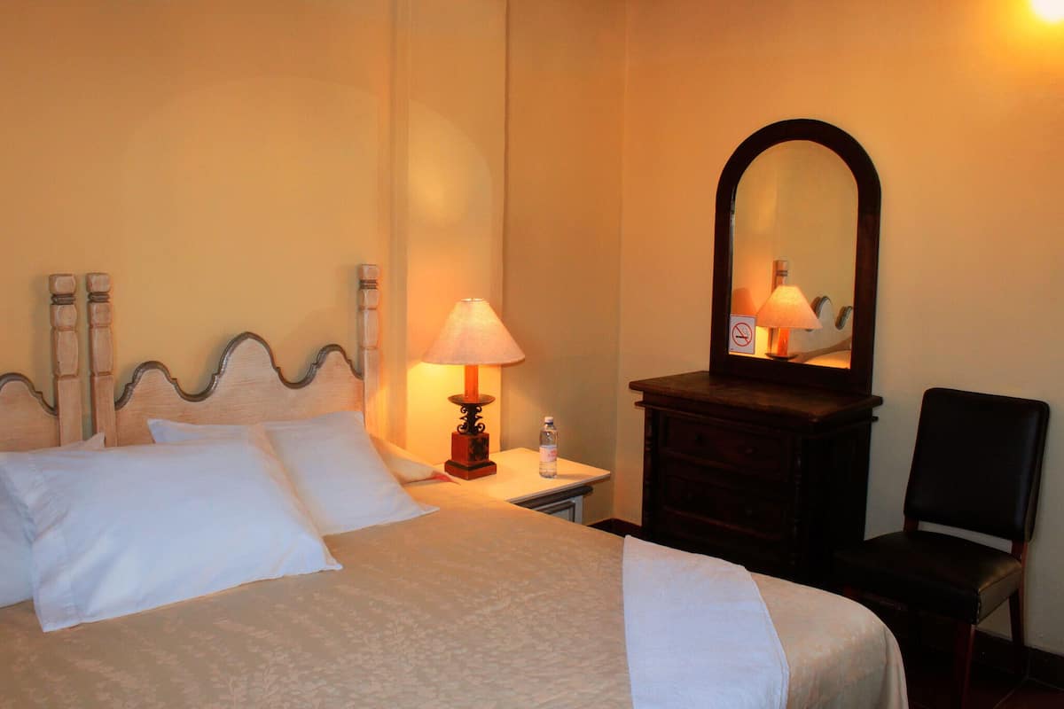 Un lit bien fait, avec des oreillers, une lampe de chevet, une commode et une chaise, dans une chambre d’hôtel.