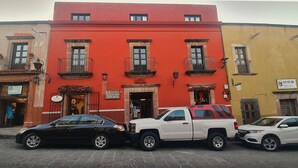 Un hôtel à la façade rouge, une voiture noire garée devant et un camion blanc garé à côté.