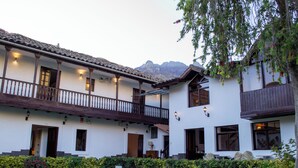 Un edificio a due piani con un balcone, un giardino curato e montagne sullo sfondo.