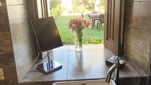 Un bagno con un lavandino bianco, un tavolino con un portatile e un vaso con fiori rosa.