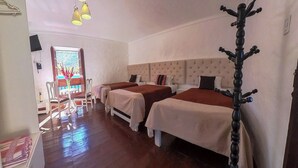 Camera d'albergo con due letti, pavimento in legno, area pranzo con tavolo e sedie e vista sull'esterno da una finestra.