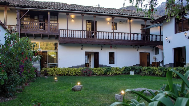 Un edificio a due piani con un balcone, un giardino con prato e un siepe curata.