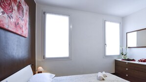 A hotel room with a bed, two windows, a dresser, and a painting on the wall. - Comfortable apartment with garden view - Treviso center (Treviso)