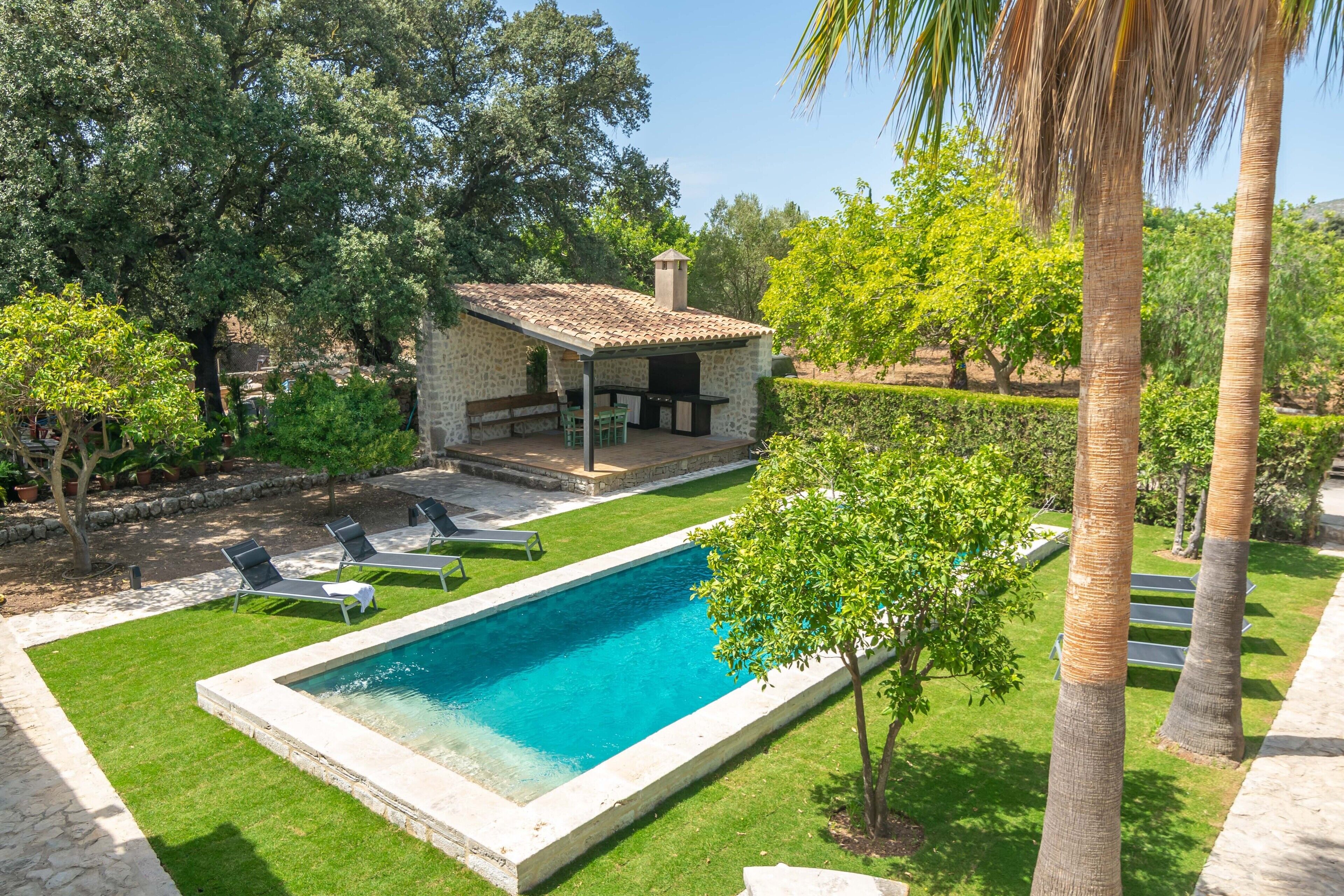 Una piscina con patio de piedra, sillas de descanso y una pequeña cocina al aire libre.