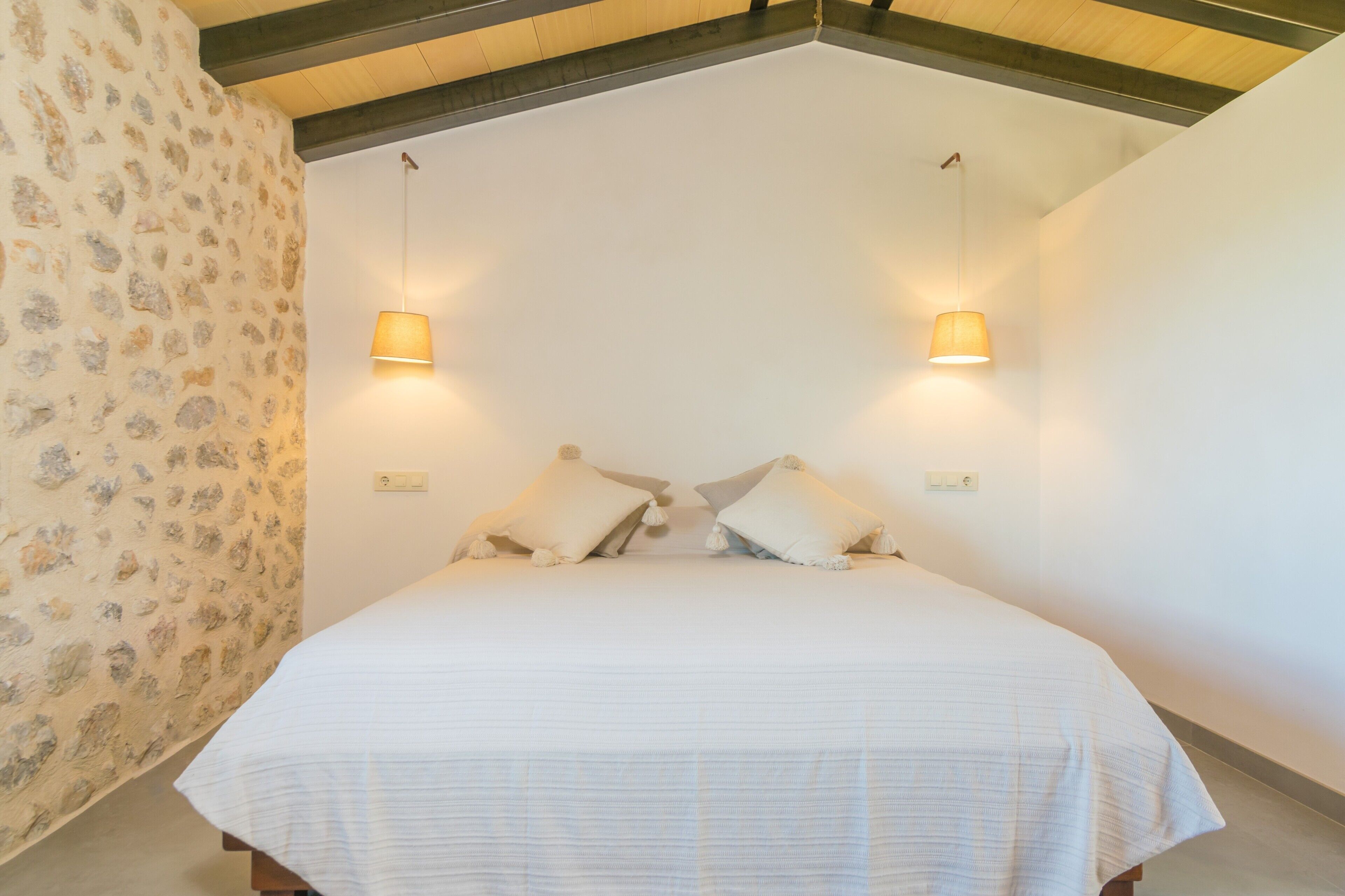 A bedroom with a large bed, two bedside lamps, and a stone-patterned wall.