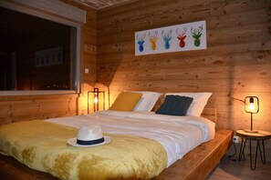 A wooden cabin-style bedroom with a large bed, a window, a painting of deer heads, and a hat on the bed. - Chalet BAMBI in GÉRARDMER for unforgettable holidays (GERARDMER)