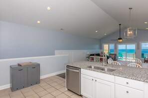 A modern kitchen with a granite countertop, white cabinetry, and a view of the ocean.
