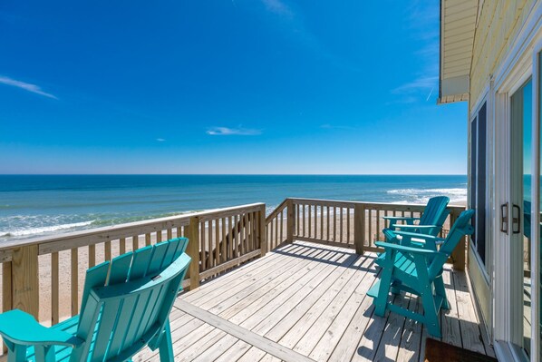 A wooden deck with a view of the ocean, featuring two chairs and a door.
