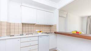 Cozinha compacta com armários brancos, máquina de lavar louça e bancada de madeira.