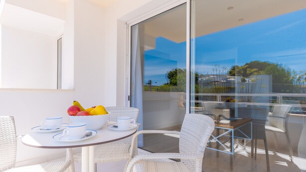 Un balcone con un tavolo apparecchiato per due, sedie in vimini bianco e una ciotola di frutta.