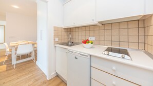 Una cucina moderna con mobili bianchi, lavastoviglie integrata e parete rivestita in piastrelle.