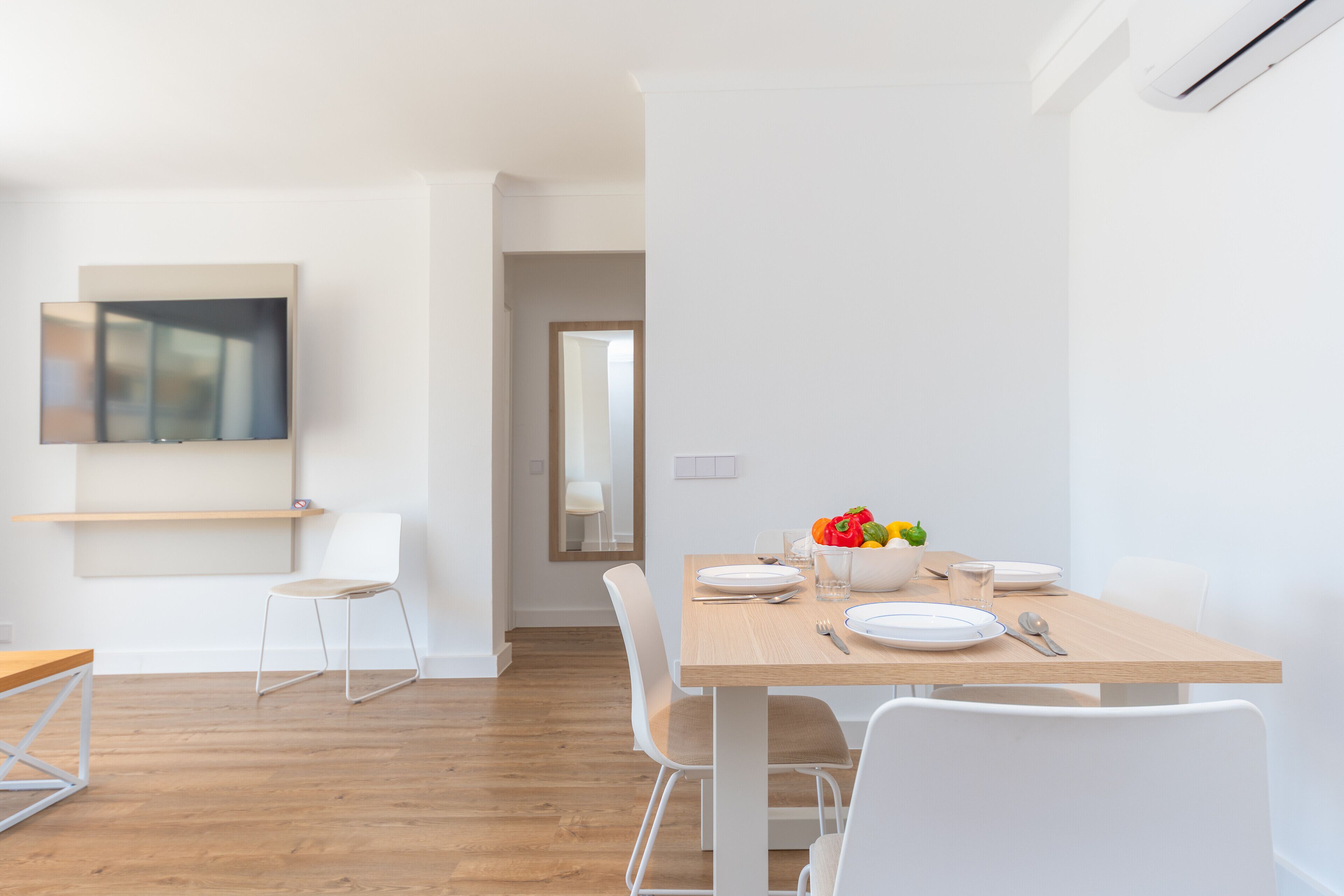 Un comedor moderno con una mesa de madera, sillas blancas y un cuenco de fruta.