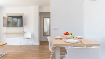 Un comedor moderno con una mesa de madera, sillas blancas y un cuenco de fruta.